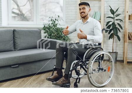 Happy smiling young man in a wheelchair at home 73657801