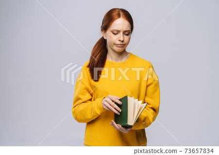 Tired young woman college student turning pages of book on gray isolated background. 73657834