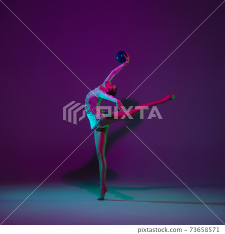 Young female athlete, rhythmic gymnastics artist on purple background with neon light. Beautiful girl practicing with equipment. Grace in performance. Young female athlete, rhythmic gymnastics artist on purple background with neon light. Beautiful girl practicing with equipment. Grace in performance. 73658571