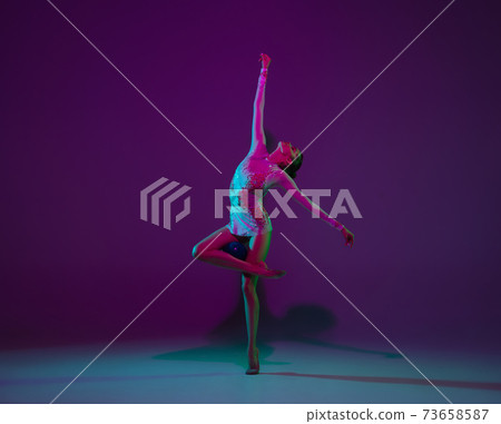 Young female athlete, rhythmic gymnastics artist on purple background with neon light. Beautiful girl practicing with equipment. Grace in performance. Young female athlete, rhythmic gymnastics artist on purple background with neon light. Beautiful girl practicing with equipment. Grace in performance. 73658587