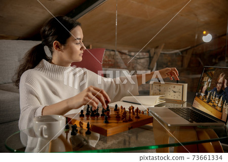 Young beautiful girl sitting at home and playing chess with friend online. Young beautiful girl sitting at home and playing chess with friend online. 73661334