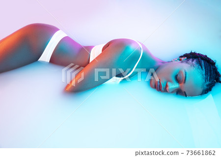 Beautiful female body in the milk bath with soft glowing in blue-pink neon light Beautiful female body in the milk bath with soft glowing in blue-pink neon light 73661862