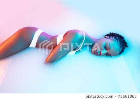 Beautiful female body in the milk bath with soft glowing in blue-pink neon light Beautiful female body in the milk bath with soft glowing in blue-pink neon light 73661863