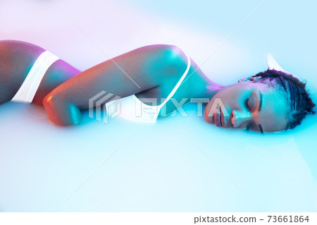 Beautiful female body in the milk bath with soft glowing in blue-pink neon light Beautiful female body in the milk bath with soft glowing in blue-pink neon light 73661864