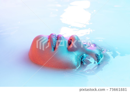 Beautiful female face in the milk bath with soft glowing in blue-pink neon light 73661881