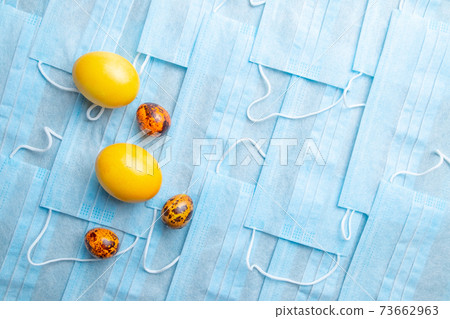 COVID-19 Flat lay. Colored Easter eggs on a background of blue medical masks COVID-19 Flat lay. Colored Easter eggs on a background of blue medical masks 73662963