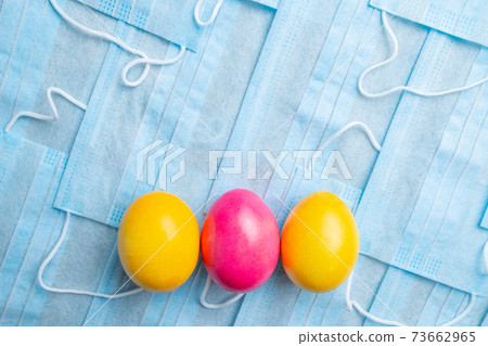 COVID-19 Flat lay. Colored Easter eggs on a background of blue medical masks COVID-19 Flat lay. Colored Easter eggs on a background of blue medical masks 73662965
