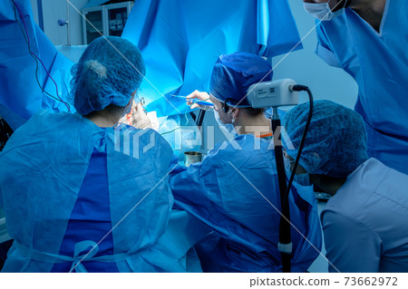 A group of surgeons performing minimally invasive surgery on the patient's anus using surgical instruments.  73662972