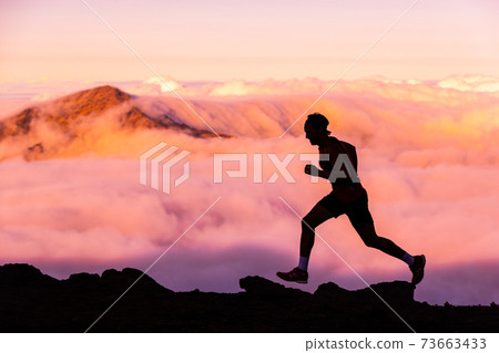 Trail runner athlete man running in nature landscape. Silhouette of male person training on mountains in cold weather with pink clouds at sunset. Amazing mountain peaks in the background Trail runner athlete man running in nature landscape. Silhouette of male person training on mountains in cold weather with pink clouds at sunset. Amazing mountain peaks in the background 73663433
