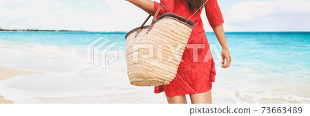 Beach bag vacation woman walking relaxing on tropical holidays holding tote purse for summer accessories for the beach. Tourist walking with red beachwear dress on travel holidays. Panorama crop. Beach bag vacation woman walking relaxing on tropical holidays holding tote purse for summer accessories for the beach. Tourist walking with red beachwear dress on travel holidays. Panorama crop. 73663489