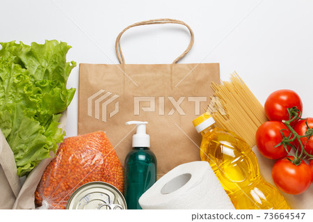 Food delivery service. Buy products online during quarantine. Healthy food and antiseptic with paper bag on white background. Salad, sunflower oil, tomatos, pasta, caned food, toilet paper, sanitizer. 73664547