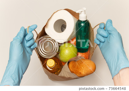 Food delivery service. Bag with donation food and sanitizer. Hands in latex gloves hold a paper bag with order. Buy online during the quarantine. Delivery service concept. High quality photo. 73664548
