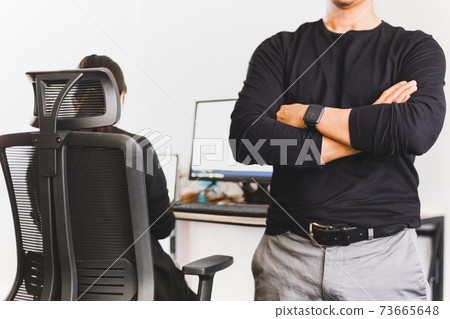 Businessman standing with his arms crossed with woman working in background. 73665648