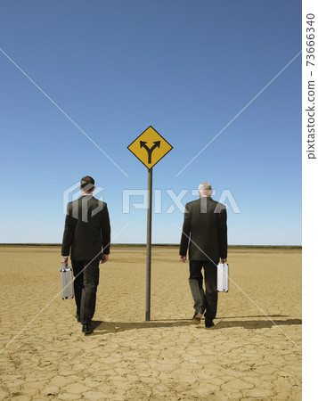 Businessmen Walking Past Road Sign In Desert Businessmen Walking Past Road Sign In Desert 73666340