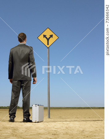 Businessman Looking At Road Sign On Desert Businessman Looking At Road Sign On Desert 73666342