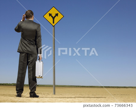 Businessman Looking At Road Sign On Desert Businessman Looking At Road Sign On Desert 73666343