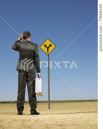 Businessman Looking At Road Sign On Desert Businessman Looking At Road Sign On Desert 73666344