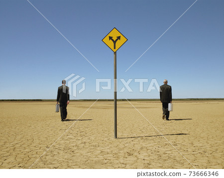 Businessmen Walking Past Road Sign In Desert Businessmen Walking Past Road Sign In Desert 73666346