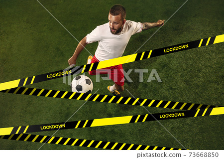 Football or soccer player on grass background behind limiting tapes with word Lockdown Football or soccer player on grass background behind limiting tapes with word Lockdown 73668850