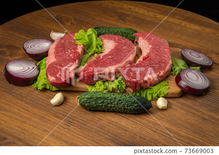 Raw marbled beef steaks with lettuce, red onion, garlic and cucumber 73669003