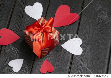 Gift box with red bow ribbon and paper hearts on wooden background for Valentines day Gift box with red bow ribbon and paper hearts on wooden background for Valentines day 73669847