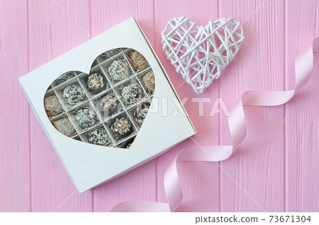 Chocolate handmade candies on pink wooden table. Chocolate box with heart and a festive ribbon. Gift for valentine's day 73671304