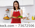 Asian woman chef in red apron holding salmon steak, serving on wooden board. Concept woman preparing meals at home. 73672506