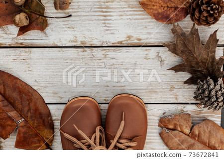 Autumn background with brown shoes and natural leaves on wooden table, seasonal pattern as mockup or banner 73672841