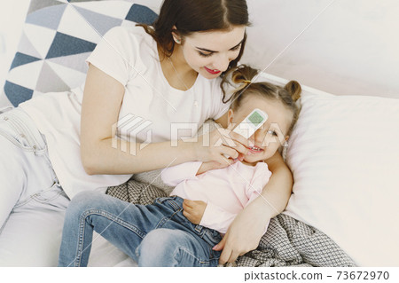 Mother with thermometer is sitting near daughter Mother with thermometer is sitting near daughter 73672970