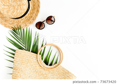 Eco rattan bag, straw hat and tropical palm leaf. Traveler accessories concept on white background. Summer background. Flat lay, top view. 73673420