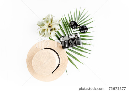 Flat lay traveler accessories on white background with retro camera, straw hat, sunglasses, and tropical palm leaf. Travel concept background.  73673877
