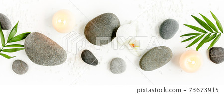 Spa stones, palm leaves, flower white orchid, candle and zen like grey stones on white background. Flat lay, top view 73673915