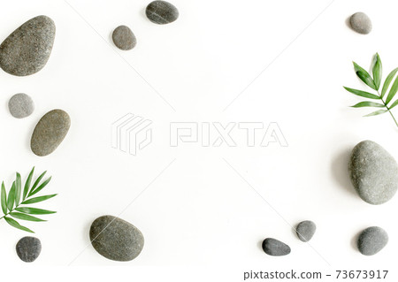 Spa stones, palm leaves, candle and zen like grey stones on white background. Flat lay, top view 73673917
