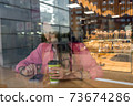 woman in a city cafe in summer reads social networks in Internet application. Background of coffee tea pastries showcase, smartphone on table. Rest and lunch after work, breakfast break. 73674286
