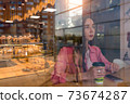 Woman in summer in a city cafe. Free space for a copy of text. Background of coffee tea pastries and showcase, smartphone on table. Rest and lunch after work, breakfast break. 73674287