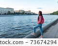 woman in summer in city stands by river bank, free space for a copy of the text, a date and meeting on the street, travel and enjoying a weekend. Lake pond and water in city. 73674294