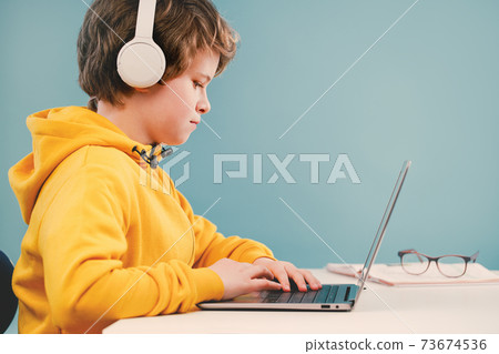 Child boy with headphones studying at home with laptop Child boy with headphones studying at home with laptop 73674536