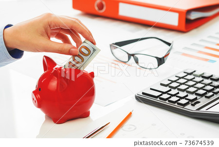 Hand putting hundred dollars note into piggy coins bank 73674539