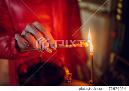 Woman's hand in a red jacket puts a church candle. 73674934