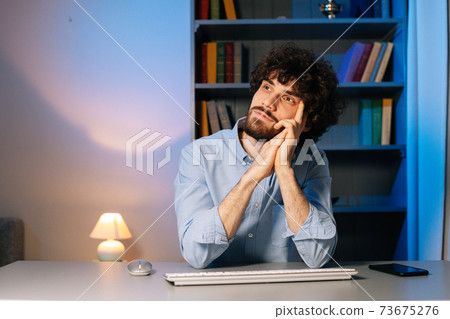 Front view of thoughtful young businessman working on computer sitting at desk Front view of thoughtful young businessman working on computer sitting at desk 73675276