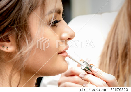 Artist's hand applying lipstick gloss Artist's hand applying lipstick gloss 73676200