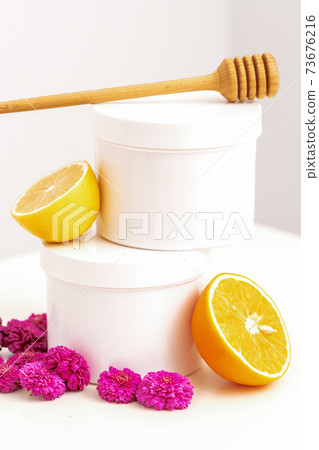 Jars with wooden honey stick, fresh lemon and flowers 73676216