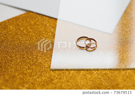 Two golden wedding rings on a golden background 73679515