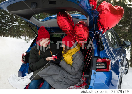 Valentine Gift. Happy Young Couple with Valentine's Day or birthday present. Happy Man giving a gift to his Girlfriend. Love concept. Couple sitting in car trunk Valentine Gift. Happy Young Couple with Valentine's Day or birthday present. Happy Man giving a gift to his Girlfriend. Love concept. Couple sitting in car trunk 73679569