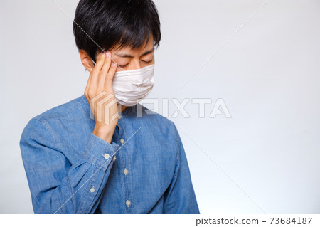 A man wearing a mask and holding his head cold migraine A man wearing a mask and holding his head cold migraine 73684187