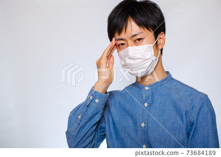 A man wearing a mask and holding his head cold migraine 73684189