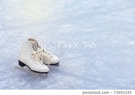 A pair of White Figure Skates are standing on an open ice rink. Winter sport A pair of White Figure Skates are standing on an open ice rink. Winter sport 73692285