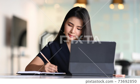 Businesswoman working with tablet computer and concentrate writing in formation on notebook. Businesswoman working with tablet computer and concentrate writing in formation on notebook. 73692850