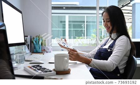 Side view of cheerful artist woman working on art projects at her workstation. 73693192