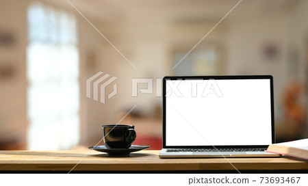 Photo of white blank screen laptop, black coffee cup and coasters on the wooden working desk over blurred modern cafe background. Photo of white blank screen laptop, black coffee cup and coasters on the wooden working desk over blurred modern cafe background. 73693467